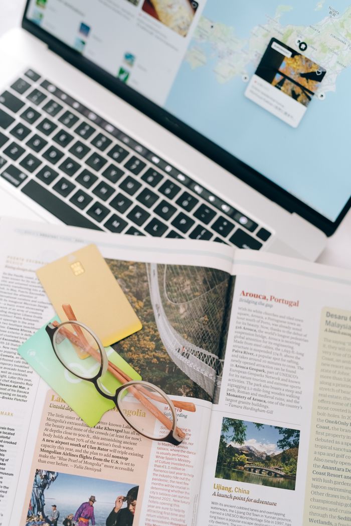 Open magazine with eyeglasses and cards next to a laptop, ideal for travel planning themes.